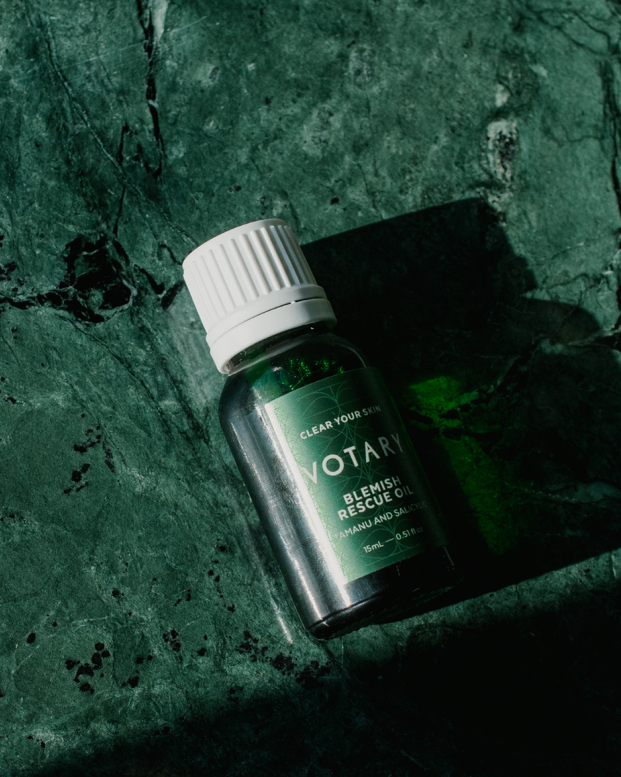 Close up of Votary Blemish Rescue Oil bottle laying on green counter.